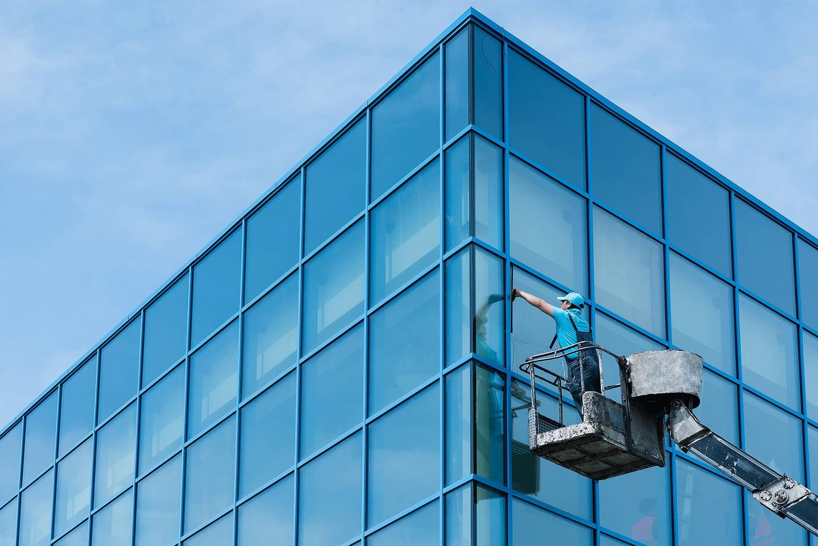 Mann reinigt mithilfe eines Kranes die Fenster einer Glasfassade